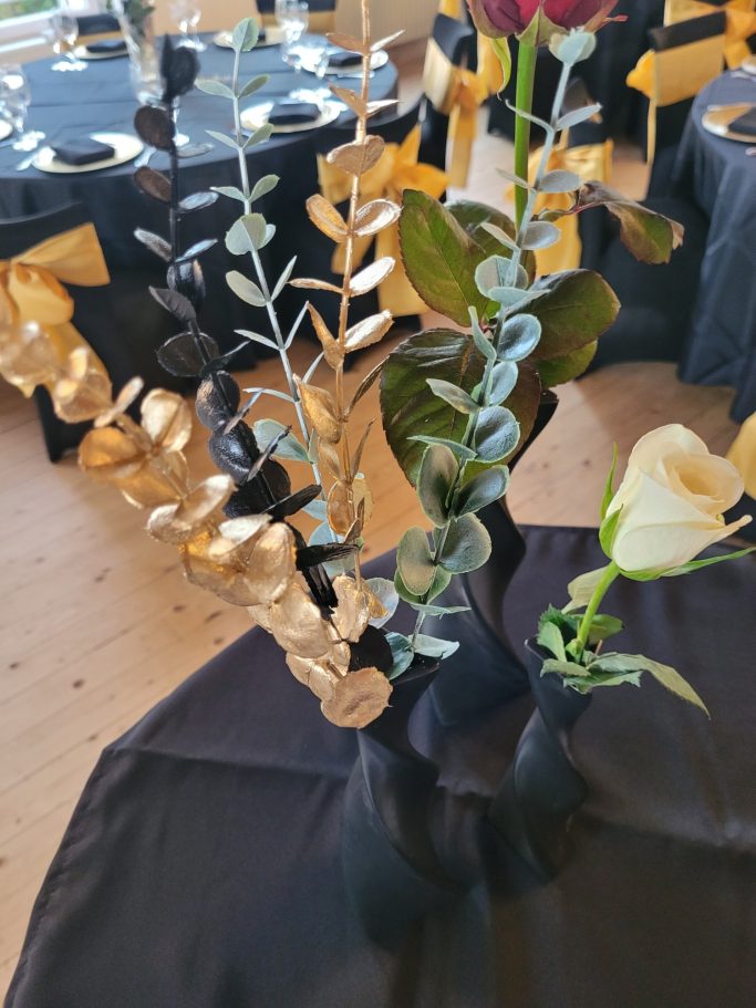 Tischdekoration mit schwarzen und goldenen Zweigen sowie weißen und roten Blumen auf schwarzem Tuch.